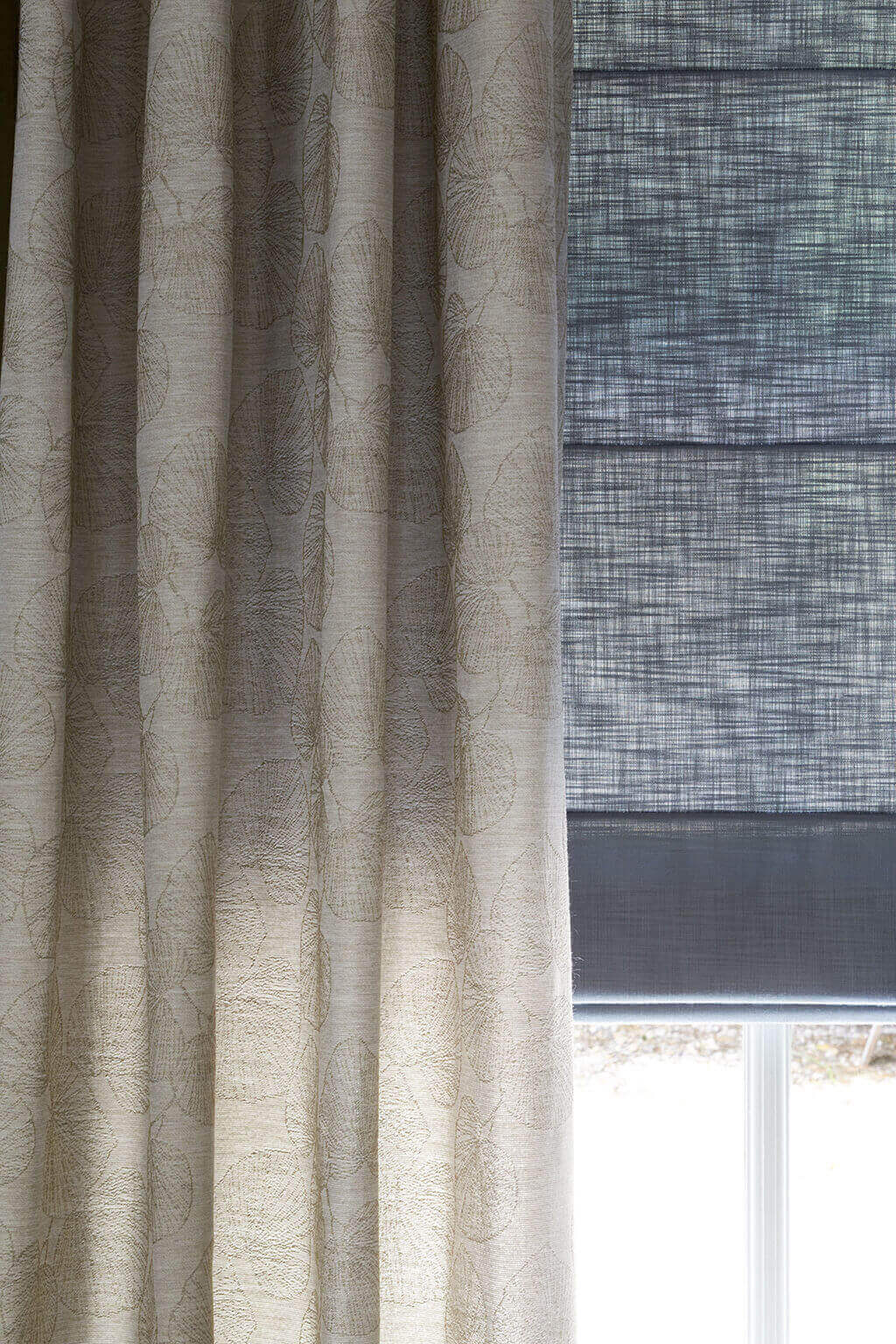 Detailaufnahme von beiger Gardine mit Blättermuster in Kombination mit einem grauen Faltrollo mit Querstreben