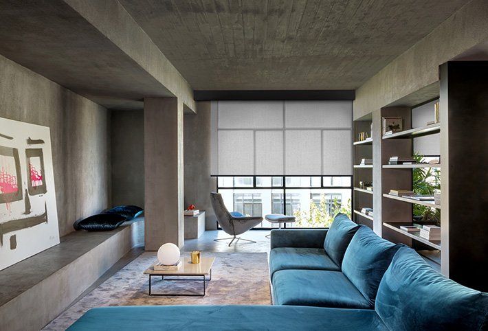 Großes Wohnzimmer mit blauem Sofa und großer Fensterfront: daran Apple Rollo montiert.