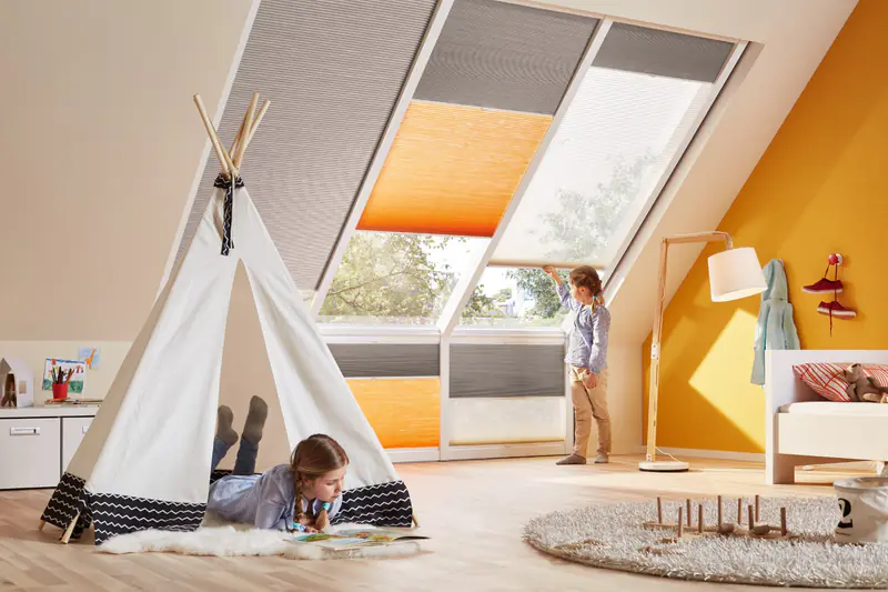 Graue, orange und weiße Wabenplissees an Dachfenstern im Kinderzimmer